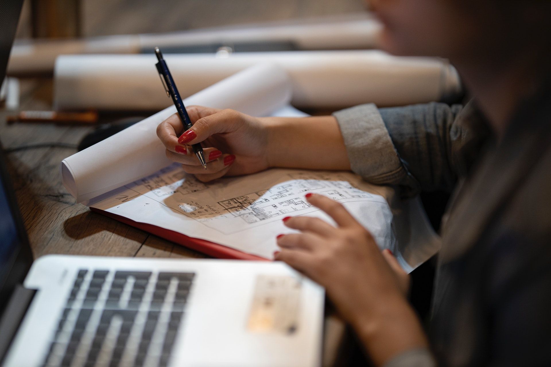 A person engaged with a laptop, analyzing blueprints laid out on the table